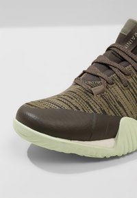 Scarpa atletica marrone con tomaia in tessuto a righe e soletta in gomma. Presenta una punta rotonda, dettagli testurizzati e un design con lacci.