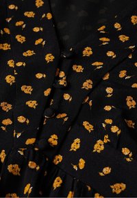 Robe en tissu noir avec un petit motif floral orange, dotée d'une fermeture à boutons et de détails froncés à la taille. Texture lisse.