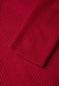 Tessuto a maglia ribbato rosso con linee verticali, caratterizzato da una texture morbida e sezioni drappeggiate per un aspetto stratificato.