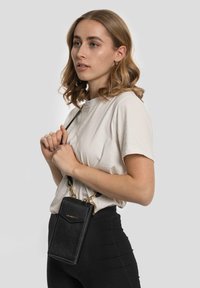 Borsa a tracolla nera in pelle con superficie testurizzata, dettagli in oro e forma rettangolare, indossata su una tracolla.