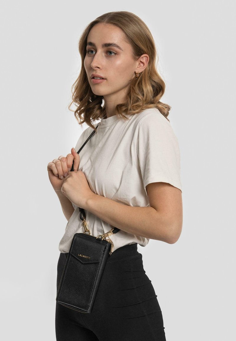 Borsa a tracolla nera in pelle con superficie testurizzata, dettagli in oro e forma rettangolare, indossata su una tracolla.