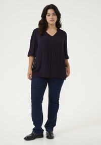 Blusa oversized de color púrpura oscuro con escote en V, manga tres cuartos y tejido suave; combinada con jeans azul oscuro y mocasines negros.