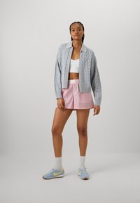 Light gray knitted cardigan with a collar, worn over a white crop top. Pink and white striped shorts. Blue sneakers with yellow accents.