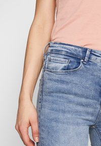 Jeans de mezclilla azul claro con un lavado desgastado, que cuentan con un bolsillo frontal y detalles de costura visibles. Combinados con una blusa rosa.