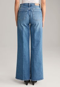 Wide-leg blue denim jeans with a medium wash, featuring a high waist, back pockets, and a leather logo patch on the waistband.