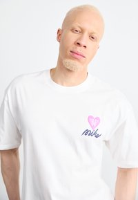 Camiseta de algodón blanca con un gráfico en el pecho que presenta un corazón rosa y la palabra "mike" en un script azul. Diseño clásico de cuello redondo.