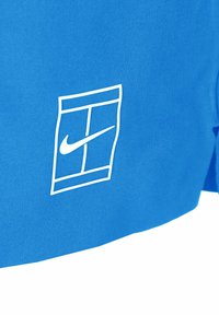 Kék Nike póló fehér logóval, téglalap alakú mintázattal, sima anyagból készült. A pólón rövid ujjak találhatók, és laza fazonú.