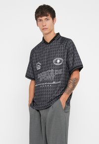 Svart kortermet skjorte med diamantmønster, med svart krage, hvite grafiske logoer og teksttrykk. Løs passform.