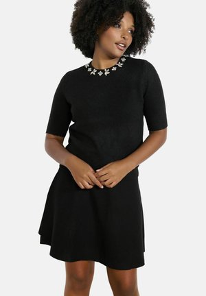 Schwarzes Strickkleid mit kurzen Ärmeln, verziert mit floralen Elementen am Ausschnitt. A-Linien-Silhouette und strukturierter Stoff.