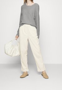 Grijze geribde lange mouw sweater, crèmekleurige losse broek, beige gevlochten mules en witte leren handtas. Eenvoudige en casual outfit.