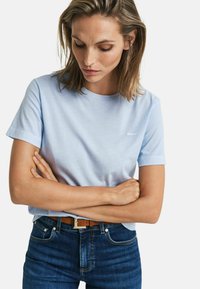Lyseblå kortærmet t-shirt lavet af blødt bomuld, med rund hals og diskret logo på brystet, parret med mørke jeans.