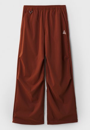 Bredde, rustfargede tekniske bukser. Laget av lett stoff, med elastisk midjebånd og sidelommer, med en logo aksent på venstre hofte.