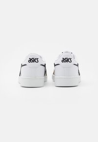 Baskets blanches avec des accents et des coutures noires, tige texturée, bout rond et semelle plate en caoutchouc blanc ; présente le logo ASICS au talon.