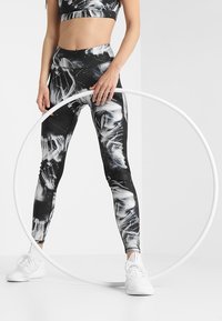 Legginsy w czarno-białe wzory i pasujący top crop, wysoki stan, elastyczny materiał; modelka trzyma białą hula hoop; białe sneakersy.
