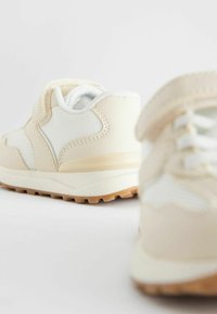 Jasne beżowe sneakersy z siateczkowymi panelami, teksturowaną gumową podeszwą i rzepem. Okrągły kształt noska z wyściełanym kołnierzem.