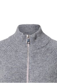 Grauer gestrickter Pullover mit gerippter Textur und einem silbernen Reißverschluss, der bis zu einem hohen, umgeschlagenen Kragen reicht.
