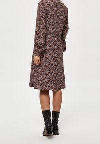 Robe à manches longues avec un motif floral aux teintes rouges, noires et blanches. Le matériau semble léger ; l'ourlet atteint le mollet.
