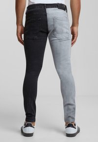 Jeans de mezclilla bicolor que presentan un lado izquierdo negro y un lado derecho gris claro, con un corte ajustado y bolsillos traseros estándar.