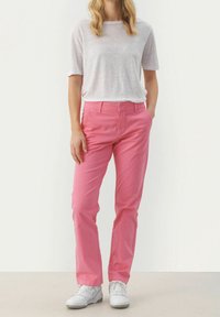 Rosa, raka byxor med en slät yta, kombinerade med en ljusgrå kortärmad skjorta och vita sneakers. Enkelt mönster, inga tryck.