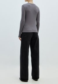 Maglia grigia a costine a maniche lunghe abbinata a jeans neri a gamba larga a vita alta. La maglia presenta un collo rotondo e una silhouette aderente.