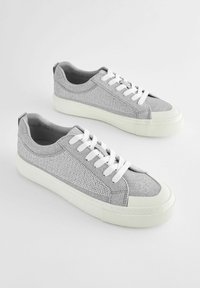 Grå sneakers i stickad tyg, med vita snören, en vit gummisula och nätdetaljer på sidorna.