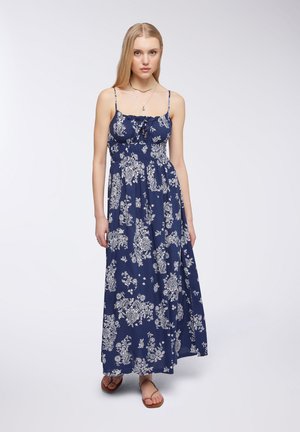 Abito lungo di colore blu navy con motivi floreali bianchi, senza maniche, con scollatura arricciata, corpino aderente e gonna fluida e ampia. Indossate sandali piatti.