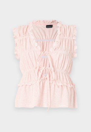 Bluzka w kolorze brzoskwiniowym z różowym odcieniem, z falbaniastymi rękawami, teksturowanym materiałem, dekoltem w kształcie litery V oraz wiązaniem z przodu. Posiada zbieraną talię i rozszerzany dół.