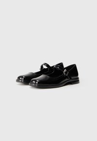 Zapatos de charol negro con punta redonda, tira estilo Mary Jane y un tacón bajo tipo bloque. Presentan un sutil detalle de costura.