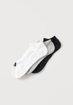 Drei Paar Knöchelsocken in Weiß, Grau und Schwarz, diagonal auf einem hellen Hintergrund gestapelt.