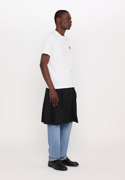 Hvit bomull T-skjorte med røde detaljer, sammen med et svart plisserte skjørt og lyseblå jeans, fullført med svarte sko.