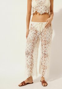 Top corto de ganchillo de encaje y pantalones de pierna ancha en blanco roto, con patrones florales y cintura con cordón. Acentuado con sandalias marrones.
