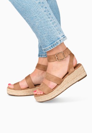 Fødder iført lyseblå jeans og tanfarvede ruskind platform sandal med ankelremme og spænde, tæerne malet pink.