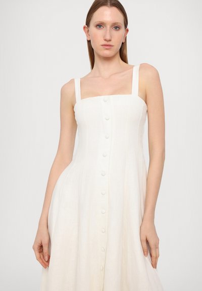 Vestido de lino blanco con escote cuadrado, tirantes finos y cierre frontal de botones. Presenta una silueta acampanada y una textura suave.