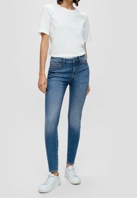 T-shirt in cotone bianco a maniche corte, abbinato a jeans blu slim-fit. Sneakers bianche completano l'outfit.