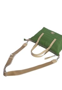 Bolsa de lona verde de nylon con asas y detalles de cuero beige. Presenta un cierre superior con cremallera, textura acolchada y un logotipo circular en la parte frontal.