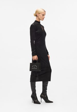 Black long-sleeved dress with a high neckline and keyhole detail, paired with black thigh-high boots and a small black handbag featuring white text.