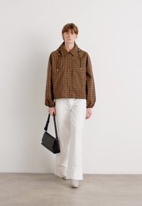 Braun kariertes Jackett mit Kragen und Ziehdrahtdetails; kombiniert mit weißen, weiten Hosen und einer kleinen schwarzen Handtasche. Glattes, strukturiertes Material.