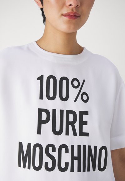 Baltos trumpomis rankovėmis marškinėliai su ryškiu juodu tekstu "100% PURUS MOSCHINO." Minkšta medžiaga, laisvas kirpimas ir apvalus kaklas.
