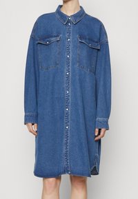 Denim shirt dress in a medium blue hue, featuring a button front, collar, two chest pockets, and long sleeves with cuffs.