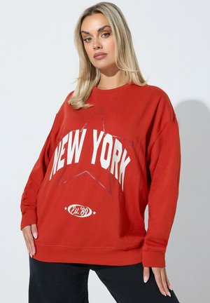 Röd oversized sweatshirt med en vit "NEW YORK"-tryck med en stjärnbakgrund och texten "Est. '89" längst ner i en cirkulär design.
