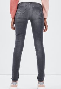 Jeans de denim gris ajustados, con bolsillos traseros, textura suave y ligero desgaste. Combinados con zapatillas blancas y grises.