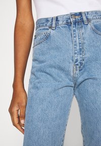 Džínové kalhoty s vysokým pasem v modré barvě se světle modrým vypráním, kontrastním šitím, předními kapsami a jedním knoflíkovým zapínáním.