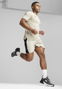 Camiseta atlética de color beige claro y pantalones cortos, con acentos laterales negros, usados con zapatillas de correr negras y calcetines blancos de caña corta.