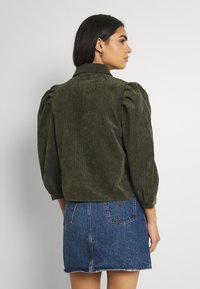 Olivengrønn kordjakke med puffede ermer, kragehals og strukturert stoff, parret med en denim mini-skjørt.