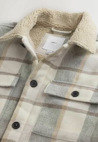Karierte Fleece-Hemdjacke in Grau, Creme und Beige. Verfügt über einen Kunstfellkragen, zwei Brusttaschen und schwarze Knopfdetails.
