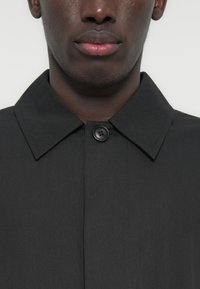 Μαύρο παλτό με κουμπιά, με κλασικό γιακά, μαλακή υφή και κλείσιμο με ένα κουμπί στον λαιμό.