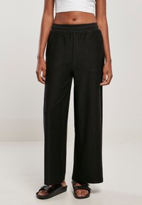 Pantalon large noir en tissu côtelé avec une taille élastique. Ils présentent une coupe décontractée et une texture lisse.