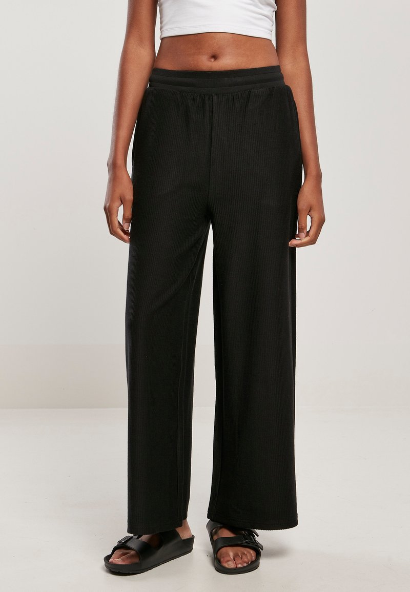Pantalon large noir en tissu côtelé avec une taille élastique. Ils présentent une coupe décontractée et une texture lisse.