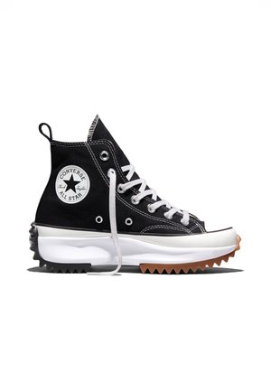 Sort høj Converse sneaker med tyk hvid sål og takkede sorte og brune slidbanemønstre, hvide snørebånd og rundt logo-mærke på siden.