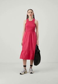 Vaaleanpunainen hihaton mekko, jossa on liehuva helma, valmistettu puuvillasta. Yhdistettynä pilkullisiin sukkiin ja tennareihin, sekä mustaan laukkuun.